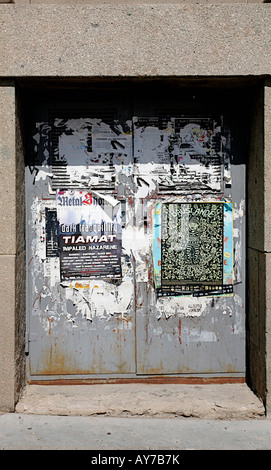 Metal doors in a small niche, have many layers of old posters peeling in various states of fading. Stock Photo