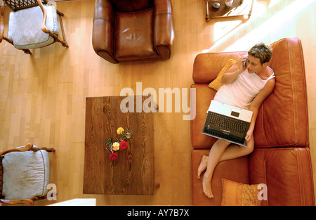 Woman working from home lying down on her settee in the living room - overhead view. Stock Photo