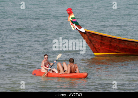 Couple in sea kayak paddle past longtail boat Ko Ngai island Thailand Stock Photo