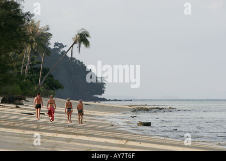 Two couples stroll on deserted beach towards sunset Ko Ngai island Thailand Stock Photo