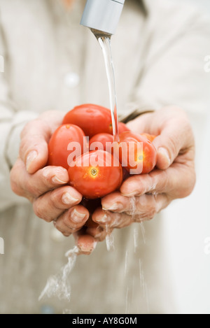 Woman rinsing handful of tomatoes under faucet, cropped view of hands Stock Photo
