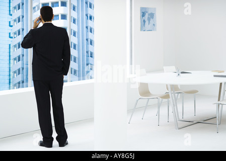 Businessman standing, looking out window, using cell phone Stock Photo
