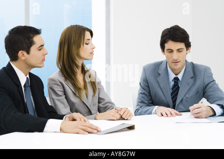 Business associates in meeting, man signing document while others watch Stock Photo