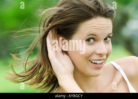 Teenage girl holding hand next to ear, looking sideways at camera, smiling, close-up Stock Photo