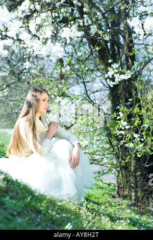 Teenage girl sitting outdoors, holding flowers, looking away Stock Photo