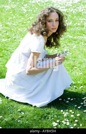 Young woman crouching in meadow, picking flowers, looking up at camera Stock Photo