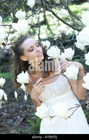 Young woman standing among tree branches, smelling flower Stock Photo