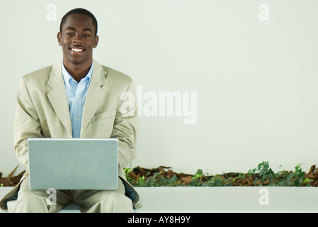 Teenage boy in suit sitting, using laptop computer, smiling at camera Stock Photo