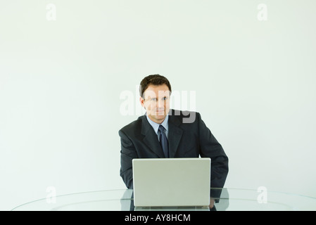 Businessman sitting at desk, using laptop computer, smiling at camera Stock Photo