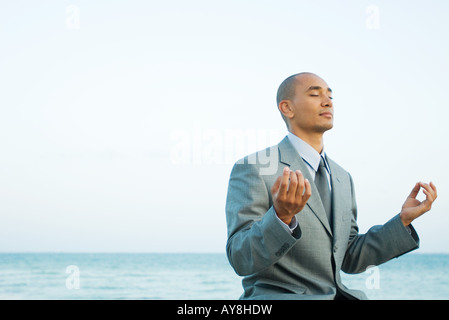Businessman sitting by the sea in lotus position, eyes closed Stock Photo