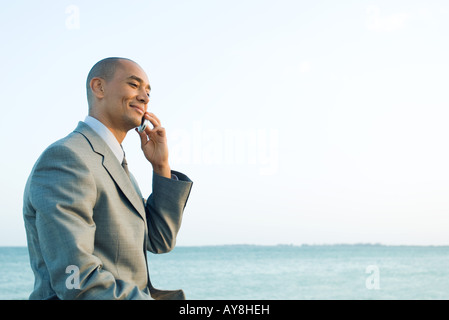 Businessman by the sea using cell phone, smiling, side view Stock Photo