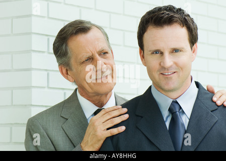 Businessman with hands on younger associate's shoulders, associate smiling at camera Stock Photo