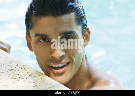Man holding on to side of swimming pool, smiling at camera, close-up Stock Photo
