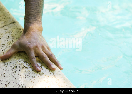 Man's hand holding side of swimming pool, close-up, cropped Stock Photo