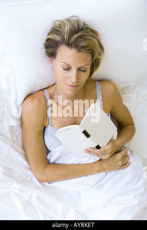 Woman asleep in bed, holding book against chest Stock Photo