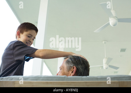 Preteen boy with hand on grandfather's head, both looking at each other, low angle view Stock Photo