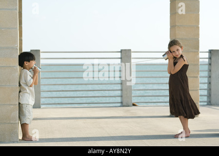 Two young friends playing with tin can phone together, sea in background Stock Photo