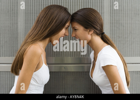 Teenage twin sisters leaning with foreheads touching, both shouting, side view Stock Photo