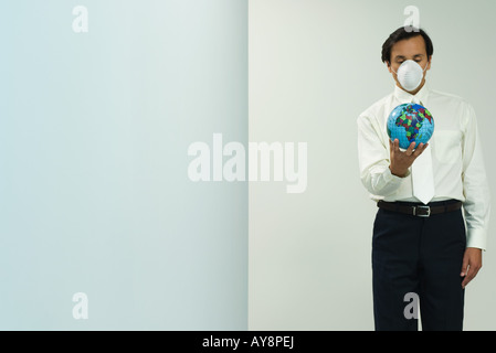 Man wearing pollution mask, holding globe, eyes closed Stock Photo
