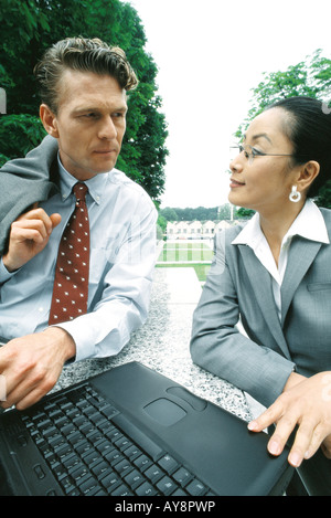 Business associates sitting outdoors, looking at each other, woman using laptop computer Stock Photo