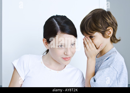 Little boy whispering in sister's ear, girl smiling Stock Photo