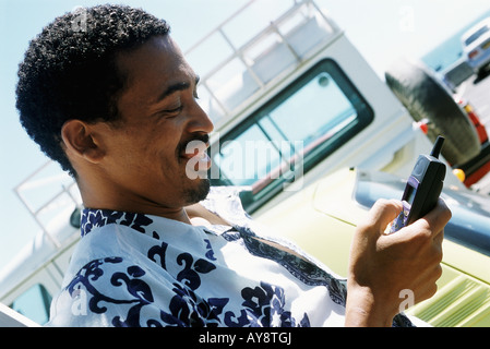 Man in Hawaiian shirt outdoors, looking down at cell phone, smiling Stock Photo