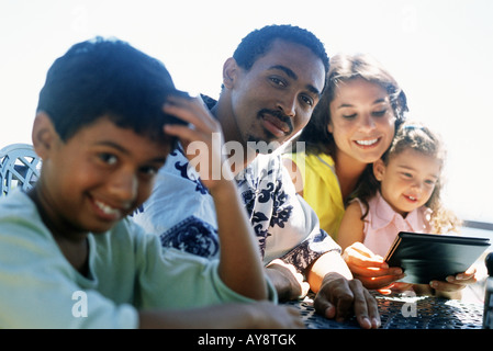 Family sitting together at table outdoors, father and son smiling at camera, mother and daughter looking at menu Stock Photo