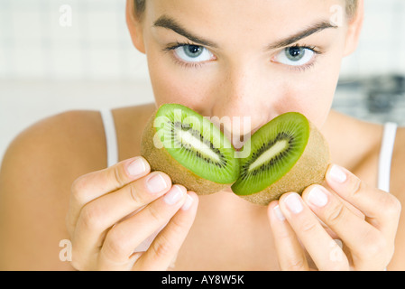 Young woman smelling freshly cut kiwi, looking at camera, close-up Stock Photo