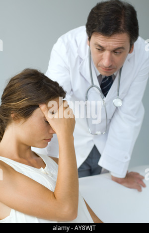 Male doctor examining patient, woman sitting with hand over eyes Stock Photo