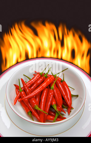 Bright red chilli peppers in a white bowl with background flames Stock Photo