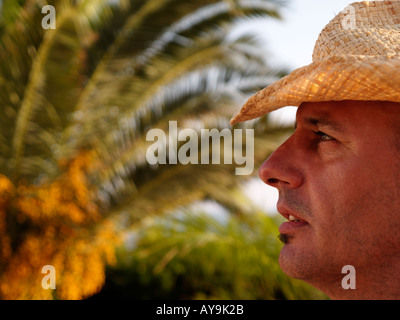 Trendy handsome good looking Male man of 35 years age, side view with straw cowboy hat and palm tree in background in sunlight Stock Photo