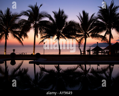 Resort swimming pool at sunrise overlooking the sea with palm trees silhouetted and reflected. Vietnam Nha Trang Stock Photo
