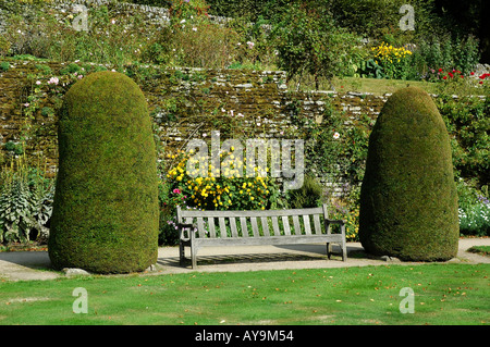 Haddon Hall wooden park bench between two conifer bushes in the gardens of the home of Lord Edward Manners Bakewell Derbyshire Stock Photo
