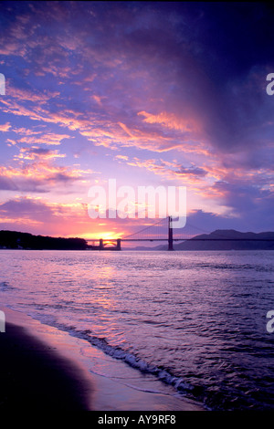 sun setting behind the Golden Gate Bridge with colorful clouds in the sky near San Francisco California Stock Photo