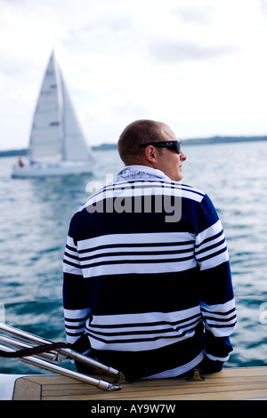 Man sitting on deck of sailing yacht, nautical fashion, Cowes, Isle of Wight, UK Stock Photo