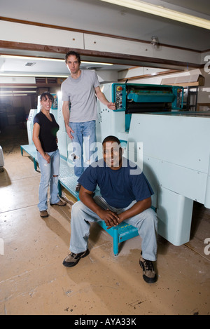 Portrait of two blue-collar men and a woman standing and sitting next two printing machines Stock Photo