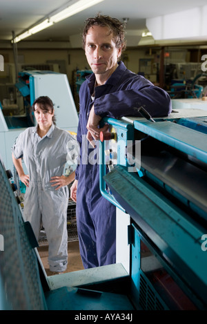 Portrait of a man and a woman in coveralls behind a printing machine Stock Photo