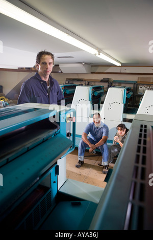 Two men and a woman in coveralls in front of a printing machine Stock Photo