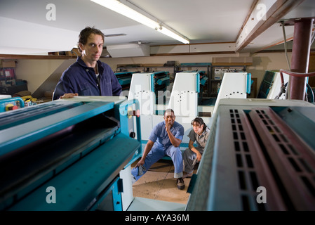 Two men and a woman in coveralls in front of a printing machine Stock Photo