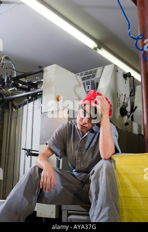 Portrait of a tired woman in coveralls sitting next to some machinery Stock Photo