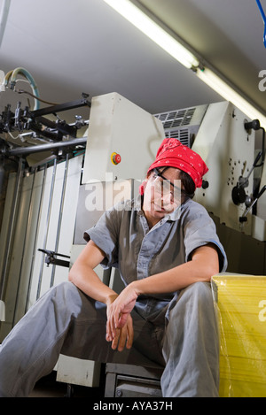 Portrait of a tired woman in coveralls sitting next to some machinery Stock Photo