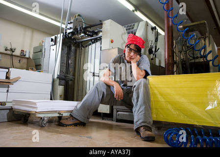 Portrait of a tired woman in coveralls sitting next to some machinery Stock Photo