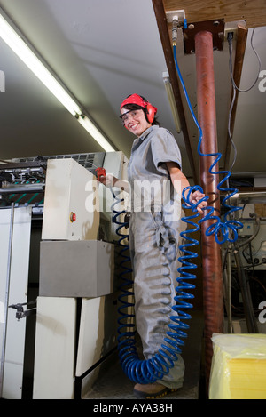 Portrait of a woman in coveralls and safety gear operating a machine Stock Photo