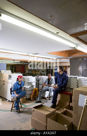 View of two men and a woman enjoying a coffee break while working in a warehouse Stock Photo
