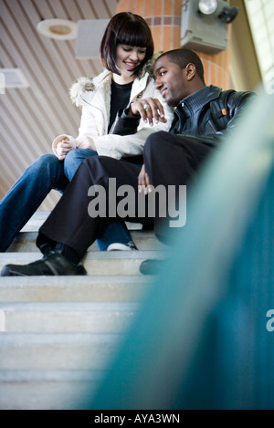 Young inter-racial couple sitting at the top of a flight of stairs at a public train station Stock Photo