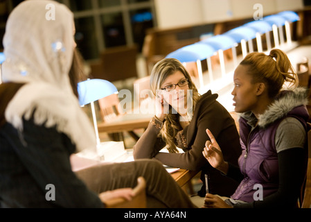 Three young women sitting and conversing in the reading room of a library Stock Photo