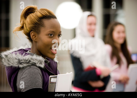 Head-shot of a young woman holding a book, while other women stand in the background Stock Photo