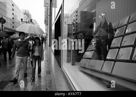 Asia Tokyo Japan Shoppers carrying umbrellas walking past department store window on rainy afternoon in Ginza District Stock Photo