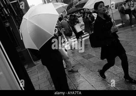 Asia Tokyo Japan Shoppers carrying umbrellas walking past department store window on rainy afternoon in Ginza District Stock Photo