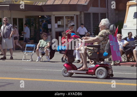 older woman riding electric wheeled chair scooter in parade Stock Photo